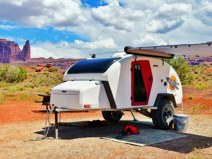 A white teardrop RV rental is parked in a vast red rock desert with a large awning deployed.. Escapod Escapod Trailer 2023