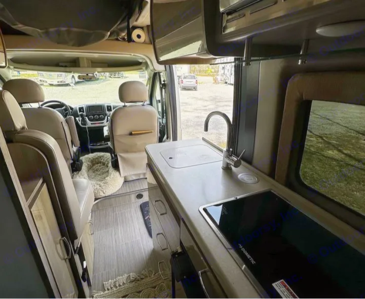 Inside this modern RV rental: compact kitchen with sink, Dometic stovetop, and cozy pet bed. Perfect for travel!. Thor Sequence 2021