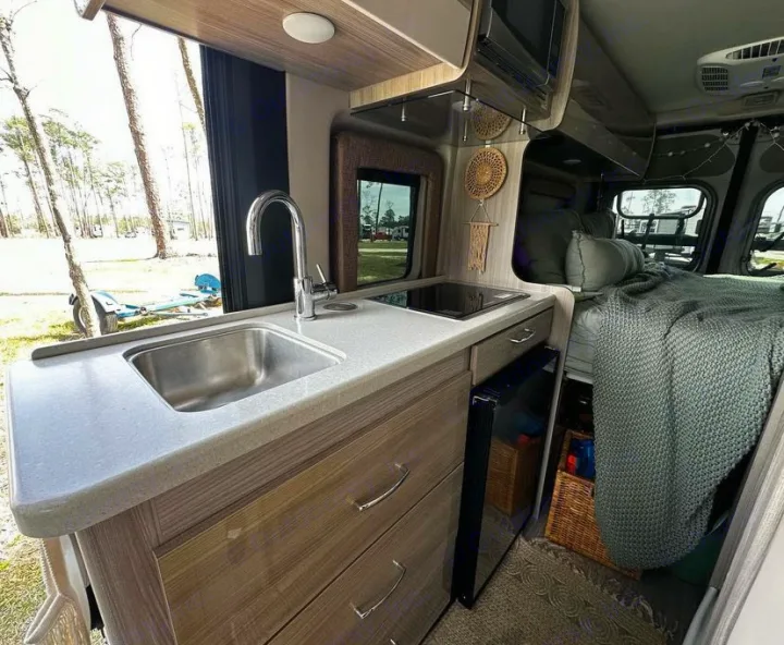 This RV rental interior boasts a compact kitchen with sink and stovetop, plus a cozy bed for your camping travels.. Thor Sequence 2021