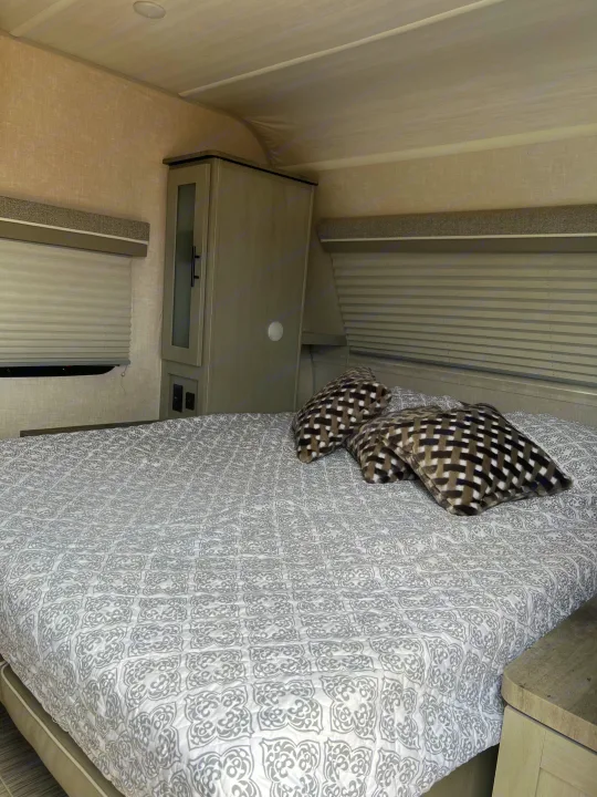 Enjoy a cozy rv rental bedroom featuring a patterned bed, two pillows, and compact storage.. Forest River Ibex 2021