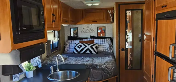 RV rental interior showcasing a compact kitchen with a sink, microwave, and a cozy bedroom area with decor.. Thor Majestic 2014