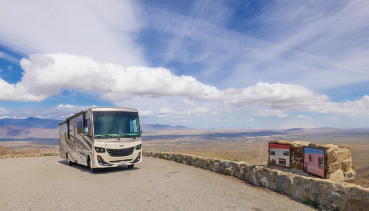 Spacious RV rental parked at a desert scenic overlook, showcasing a vast valley, distant mountains, and cloudy sky.. Fleetwood Fortis 2020