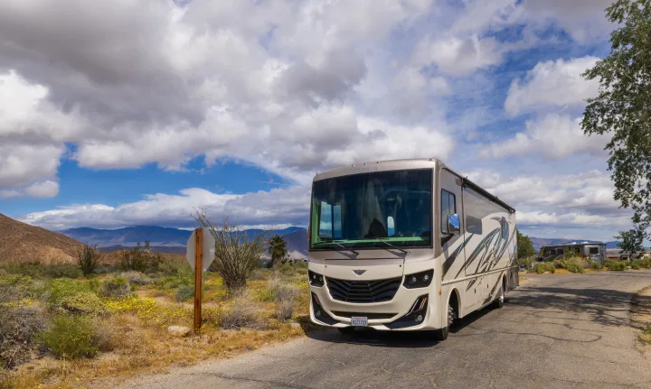 A modern beige RV rental, a Fortis motorhome, parked in a desert landscape with mountains under a partly cloudy sky.. Fleetwood Fortis 2020