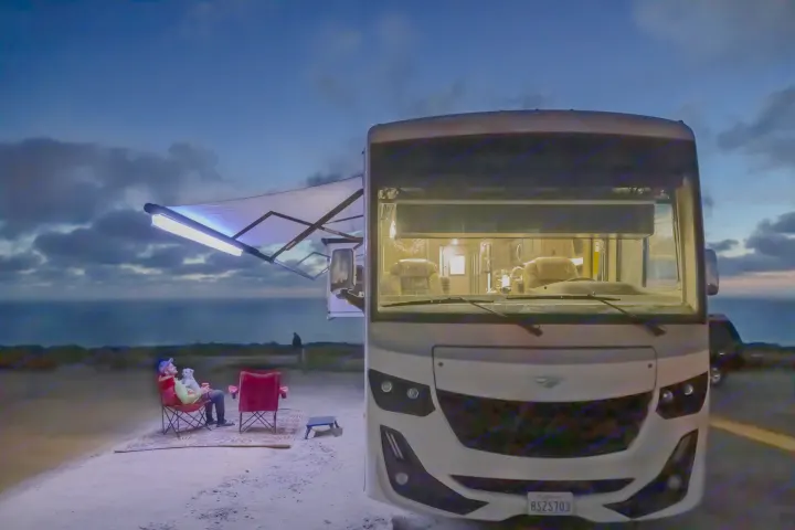 A man and his dog relaxing by an RV rental at dusk, enjoying ocean views from their coastal campsite.. Fleetwood Fortis 2020