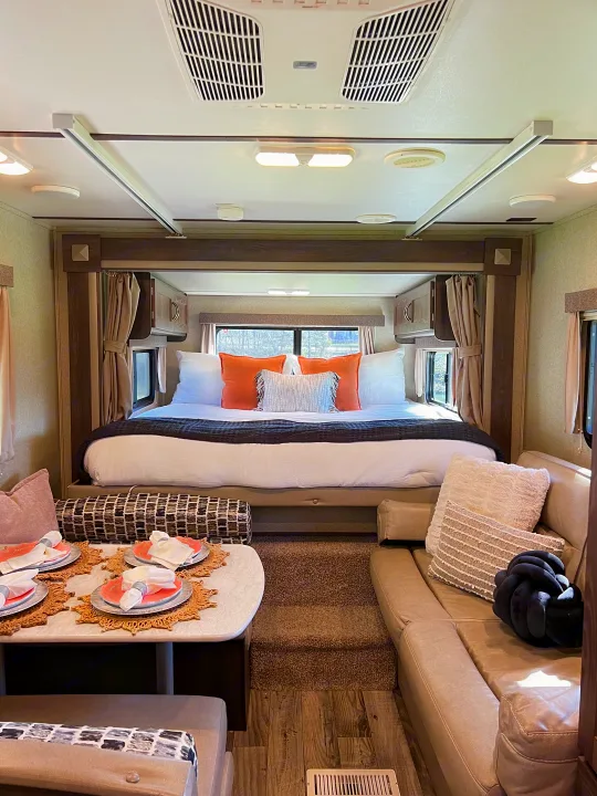 Modern RV rental interior with a spacious bedroom, dining table, and living area, featuring stylish decor and amenities.. Keystone RV Outback Ultra-Lite 2018