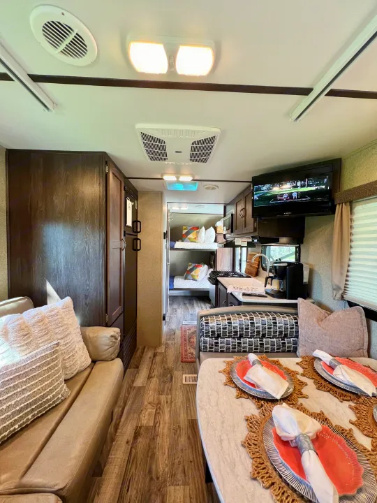 Interior view of an RV rental: living area with couch, dining table, kitchen, and bunk beds in the back.. Keystone RV Outback Ultra-Lite 2018
