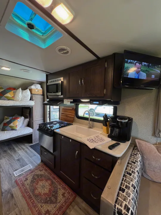 Inside this RV rental: a compact kitchen with stove, sink, microwave, Keurig, plus bunk beds and TV. Perfect for road trips!. Keystone RV Outback Ultra-Lite 2018