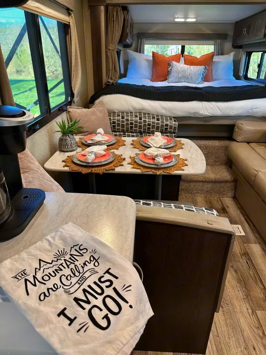 Explore this inviting RV rental interior! Cozy bedroom, complete dining setup, and kitchen area with coffee maker ready for your adventure.. Keystone RV Outback Ultra-Lite 2018