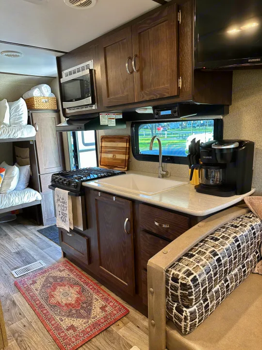 Functional RV rental interior featuring a full kitchen with stove, sink, microwave, coffee maker, and bunk beds.. Keystone RV Outback Ultra-Lite 2018