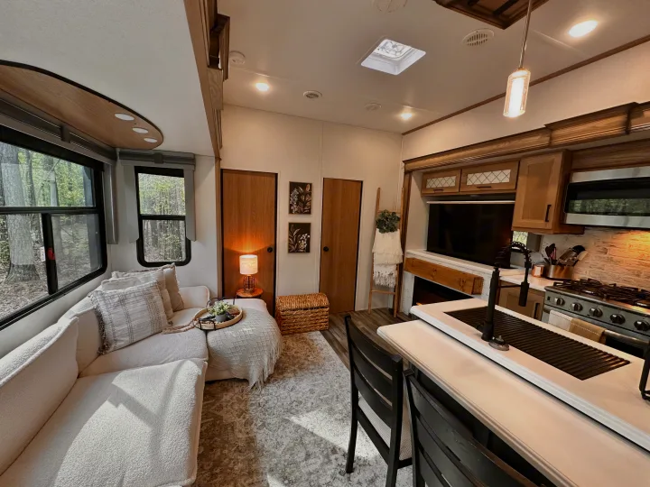 Spacious, modern RV rental interior with a comfy couch, full kitchen, and views of nature through large windows.. Primetime Sanibel 3602WB 2023