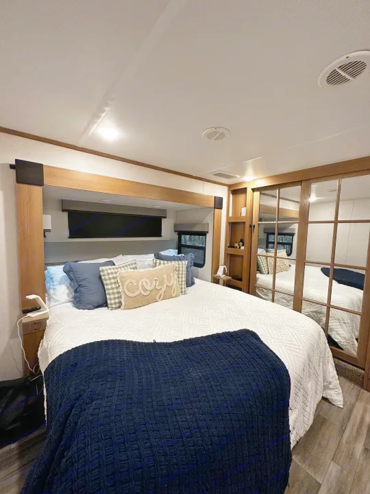 Cozy RV rental bedroom with modern wood accents, bed, and mirrored closet for comfortable stays.. Primetime Sanibel 3602WB 2023