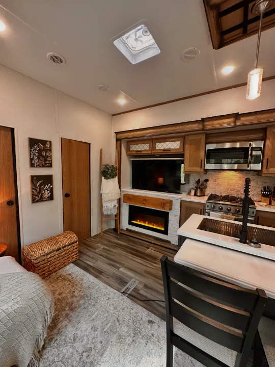 Modern RV rental interior with a cozy living area, electric fireplace, full kitchen, and partial view of bedroom.. Primetime Sanibel 3602WB 2023