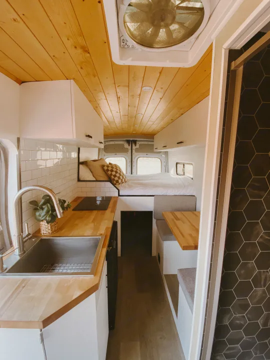 Explore this modern RV rental interior! Features a compact kitchen, cozy bed, and dining nook, ideal for travel.. Ford Transit 2020