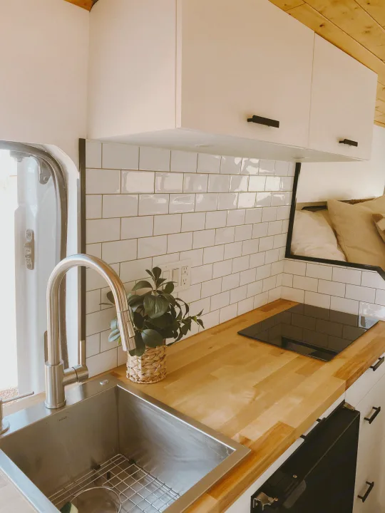 RV rental: Bright kitchen with a stainless steel sink, induction cooktop, wood counters, white subway tile, and overhead cabinets.. Ford Transit 2020