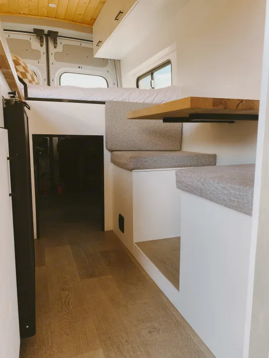 Explore the interior of this modern RV rental: a compact camper van with an elevated bed, comfy dinette, and sleek wood design.. Ford Transit 2020