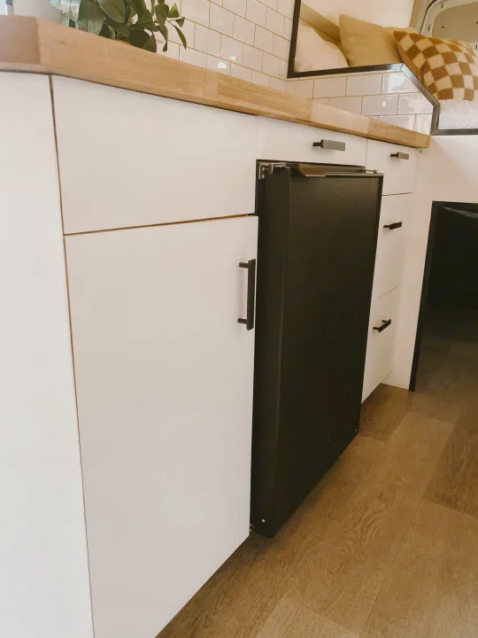 Sleek RV rental kitchen featuring white cabinets, a wooden countertop, and a built-in black refrigerator. Minimalist design.. Ford Transit 2020
