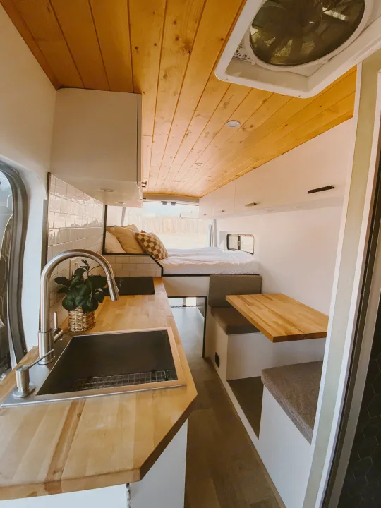 Modern camper van RV rental interior: bright kitchen, cozy bed, and dining space with wood accents. Your adventure awaits!. Ford Transit 2020