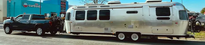 A silver Airstream travel trailer & truck, bikes loaded, parked at HEB Curbside. Explore the open road; consider an RV rental.. Airstream Globetrotter 2020