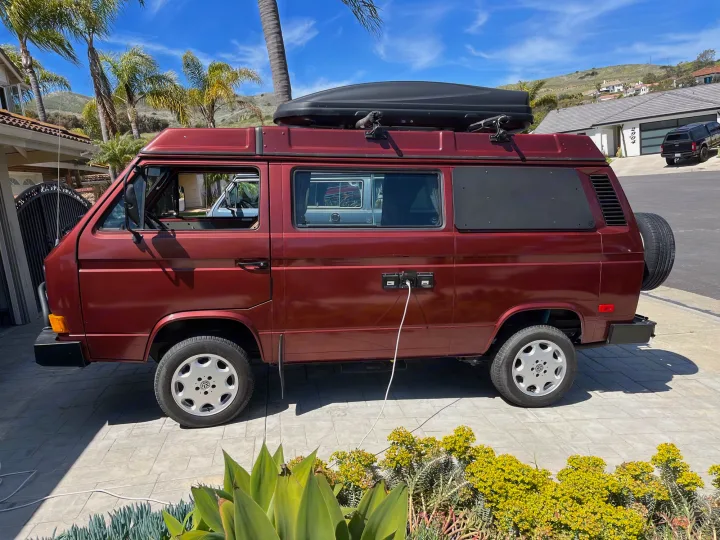 A classic red VW camper van, ideal for your next RV rental. It's parked on a sunny driveway, ready with a roof box and power.. Volkswagen Westfalia 1987