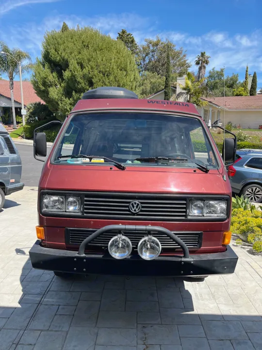 A vibrant red VW Westfalia camper van, seen from the front on a sunny day. Explore the open road with this unique RV rental.. Volkswagen Westfalia 1987