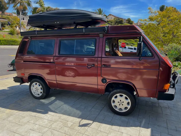 Maroon VW Vanagon camper van with roof cargo box, perfect for an RV rental adventure.. Volkswagen Westfalia 1987