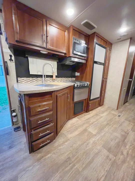 Experience comfortable travels in this RV rental kitchen, featuring dark wood cabinets, modern appliances, and a spacious counter.. Jayco Eagle HT 2018