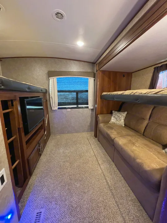 Inside an RV rental: cozy living space with sofa, upper bunk bed, TV console, and carpeted floor.. Jayco Eagle HT 2018
