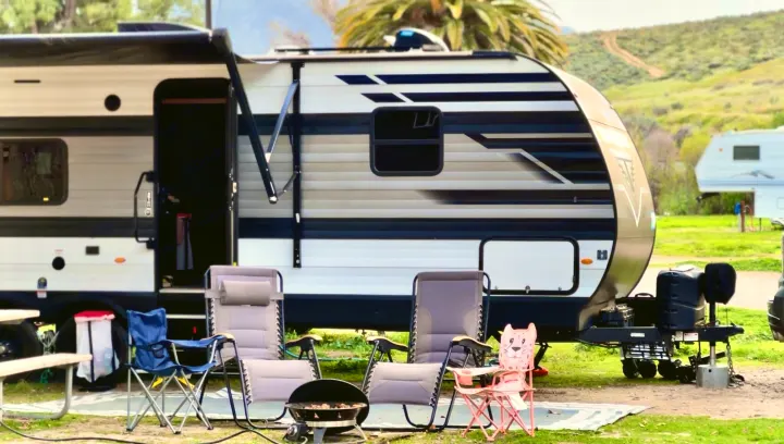 Relaxing at a scenic campsite with an RV rental, featuring an open awning, chairs, and grill. Ideal for outdoor adventures.. Grand Design Transcend Xplor 2022