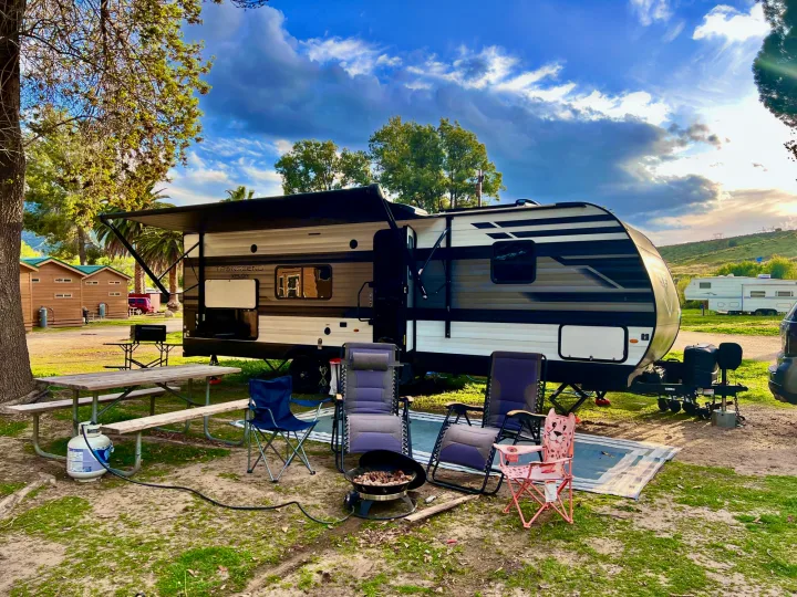 Enjoying a cozy RV rental campsite with a travel trailer, picnic table, chairs, and fire pit under a beautiful sky.. Grand Design Transcend Xplor 2022