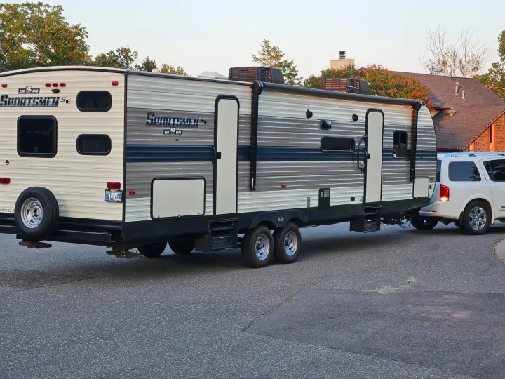 A white SUV is hitched to a large, two-tone gray and white Sportsmen RV rental, parked on a residential street.. KZ Sportsmen SE 2021