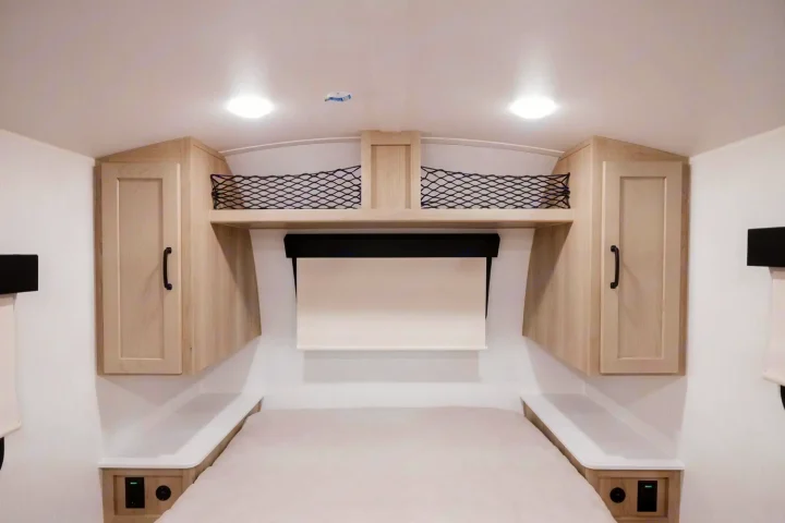 Modern RV rental bedroom with cozy bed, overhead cabinets, storage nets, and charging outlets. Ready for your adventure.. Forest River Rockwood Geo Pro 2024