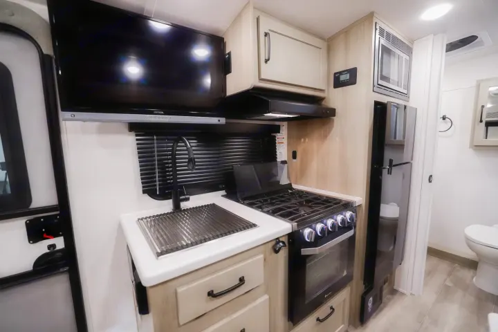 RV rental: Compact, modern kitchen with sink, stove, microwave, fridge, and a peek at the bathroom.. Forest River Rockwood Geo Pro 2024