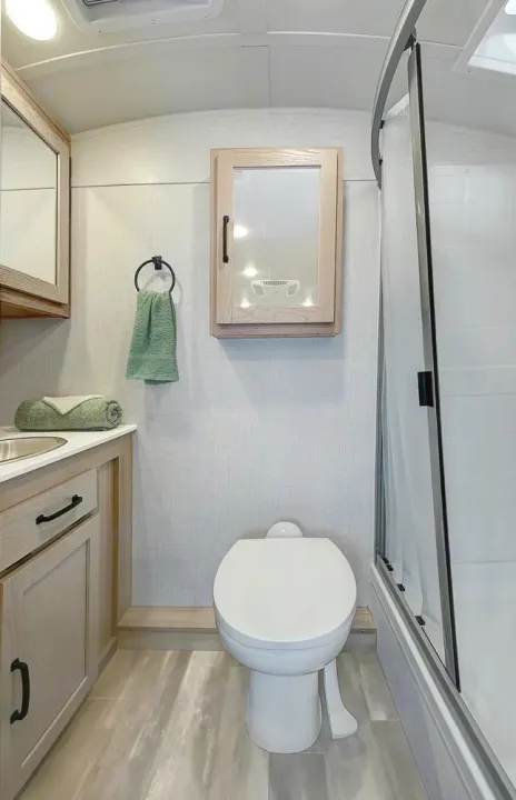 Clean RV rental bathroom with a white toilet, compact shower stall, and light wood vanity with a sink.. Forest River Rockwood Geo Pro 2024