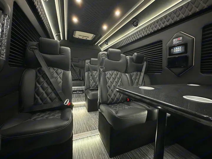 Plush black interior of an RV rental with comfortable seating, a table, and custom controls for luxury travel.. Mercedes Benz Sprinter 3500XD 2024