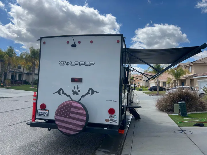 Rear view of a white Wolf Pup travel trailer RV with extended awning, parked street-side. Ideal for an RV rental getaway.. Forest River Cherokee Wolf Pup Black Label 2022