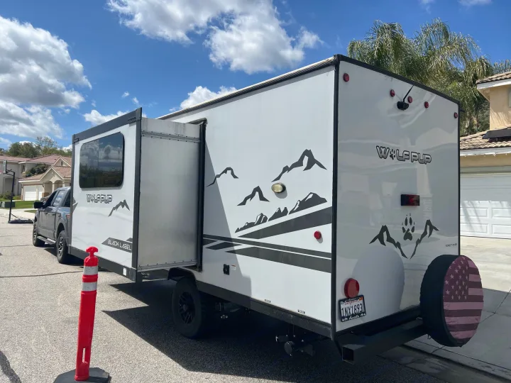 White Wolf Pup travel trailer (RV rental) hitched to a pickup truck, parked in a sunny residential driveway.. Forest River Cherokee Wolf Pup Black Label 2022