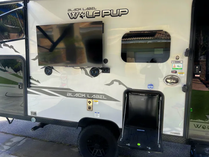A "Wolf Pup Black Label" RV rental with outdoor amenities: a mounted TV, speakers, and an accessible mini-fridge.. Forest River Cherokee Wolf Pup Black Label 2022