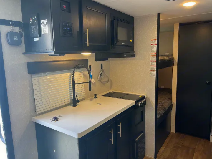 Compact RV rental interior featuring a kitchen with sink, cooktop, microwave, and visible bunk beds for a cozy stay.. Forest River Cherokee Wolf Pup Black Label 2022