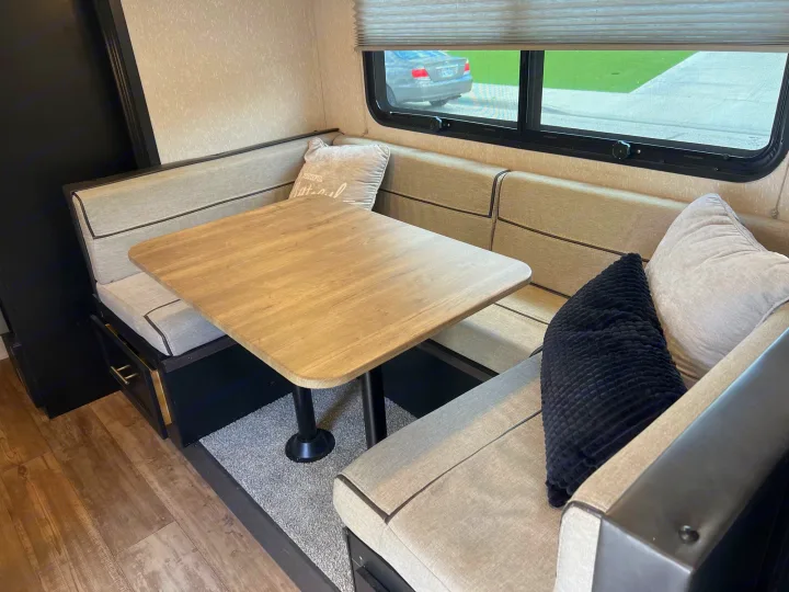 An RV rental dinette area with light-colored booth seating, a wooden table, and window views. Features under-seat storage.. Forest River Cherokee Wolf Pup Black Label 2022