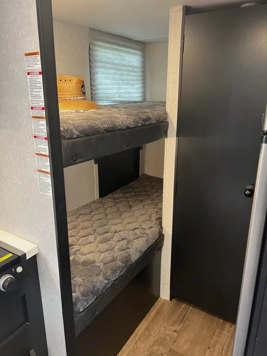 RV rental interior featuring bunk beds with cozy grey mattresses, safety warnings, and a compact design. Ideal for travelers.. Forest River Cherokee Wolf Pup Black Label 2022