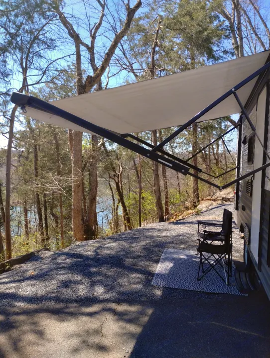 Relaxing RV rental campsite with lake view, extended awning, patterned mat, and chair set up for outdoor enjoyment.. Crossroads RV Z-1 Lite 2018