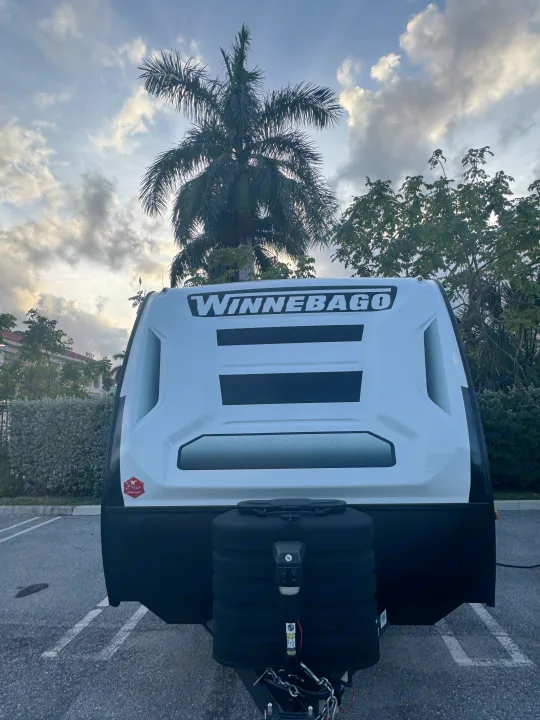 Front view of a white Winnebago travel trailer, an ideal rv rental, parked under a cloudy sky with palm trees.. Minnie Micro Minnie 2024