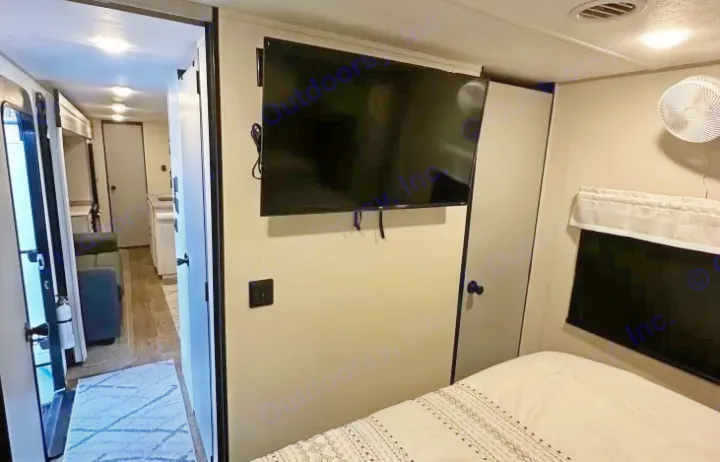 This RV rental interior features a cozy bedroom with a TV, opening into a hallway leading to the living area and kitchen.. Forest River Vibe 2022