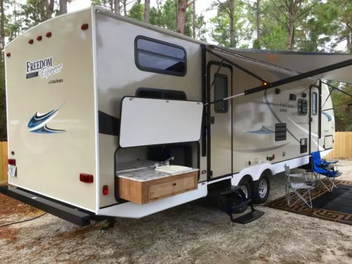 This tan rv rental features an outdoor kitchen, an extended awning with lights, and a cozy seating setup.. Coachmen Freedom Express Ultra Lite 2019