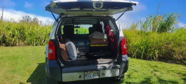 White SUV tailgate open, packed with camping gear (cooler, pillows, stove). Great for an RV rental style outdoor getaway.. Nissan Xterra 2012