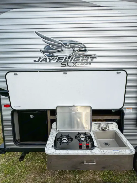 This RV rental features an outdoor kitchen with a fridge, two-burner stove, and sink, ideal for camping adventures.. Jayco Jay Flight SLX 2021
