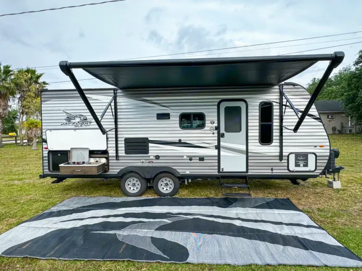 A modern Jay Flight SLX rv rental parked on grass with its awning extended, featuring an outdoor kitchen & ground mat.. Jayco Jay Flight SLX 2021