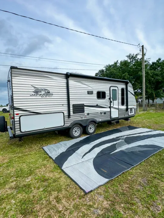 Grey Jay Flight travel trailer RV rental set up on grass with a large outdoor mat, ideal for camping.. Jayco Jay Flight SLX 2021