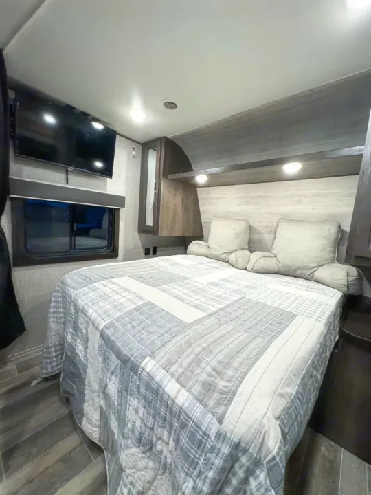 Cozy RV rental bedroom featuring a comfy bed with plaid quilt, mounted TV, and window, perfect for travel comfort.. Jayco Jay Flight SLX 2021