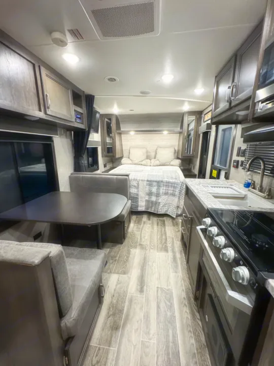 Inside a bright RV rental: cozy bed, modern kitchen with stove/sink, and dining dinette. Perfect for your travels.. Jayco Jay Flight SLX 2021